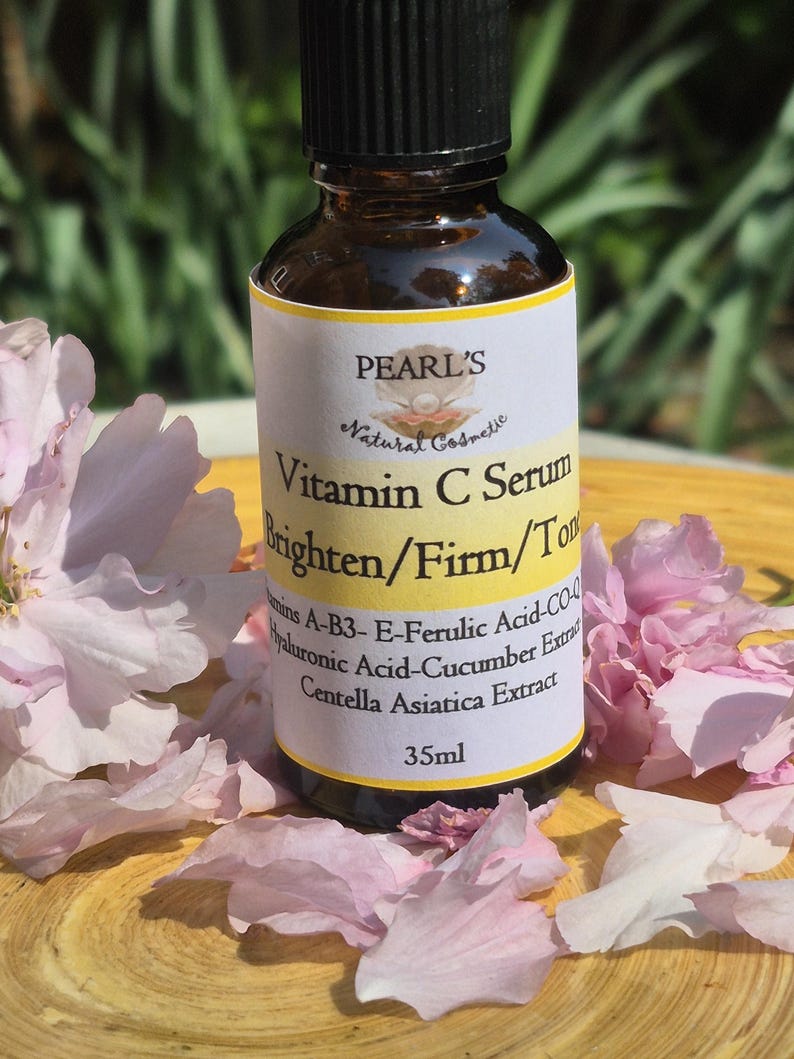 May include: A brown glass bottle of Pearl's Vitamin C Serum with a black cap, surrounded by pink flower petals. The label reads "Brighten/Firm/Tone" and lists ingredients. The bottle contains 35ml of serum.