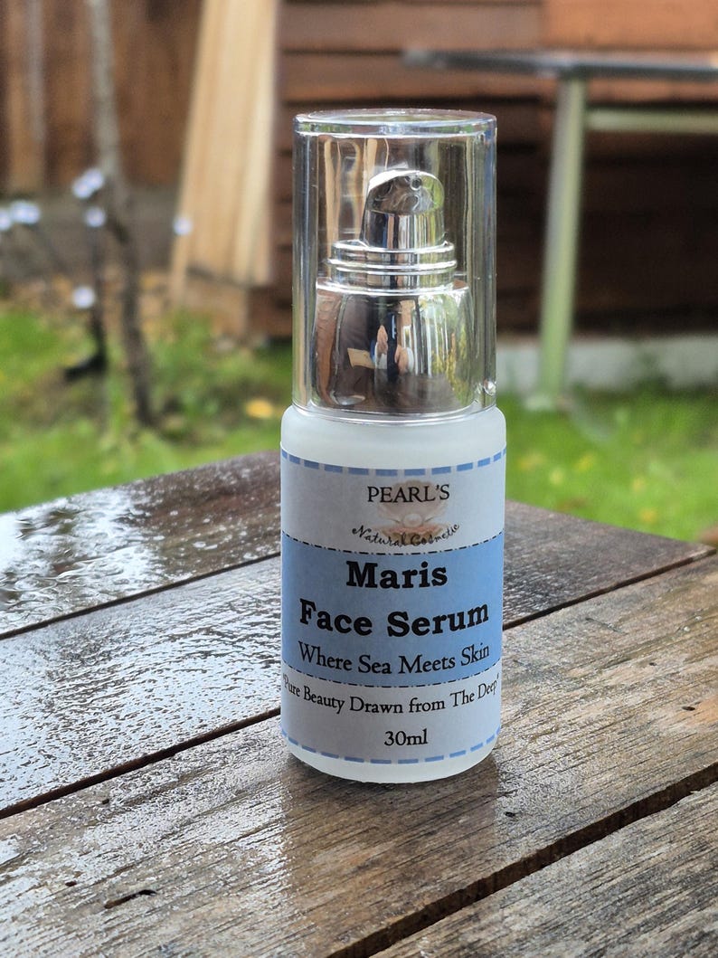 May include: A white and blue Maris Face Serum bottle with a silver pump dispenser. The label reads "Where Sea Meets Skin" and "30ml". The bottle is on a wooden surface.