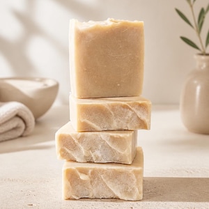 May include: A vertical stack of four rectangular bars of beige soap. Each bar features a smooth, solid surface with subtle, natural-looking variations in texture and color, showcasing a matte finish and clean, straight edges throughout the stack.
