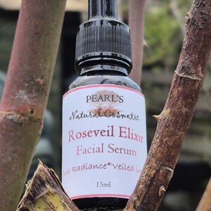 May include: A black dropper bottle of Pearl's Roseveil Elixir Facial Serum, 15ml. The label is white with red and black text. The bottle is surrounded by brown tree branches.