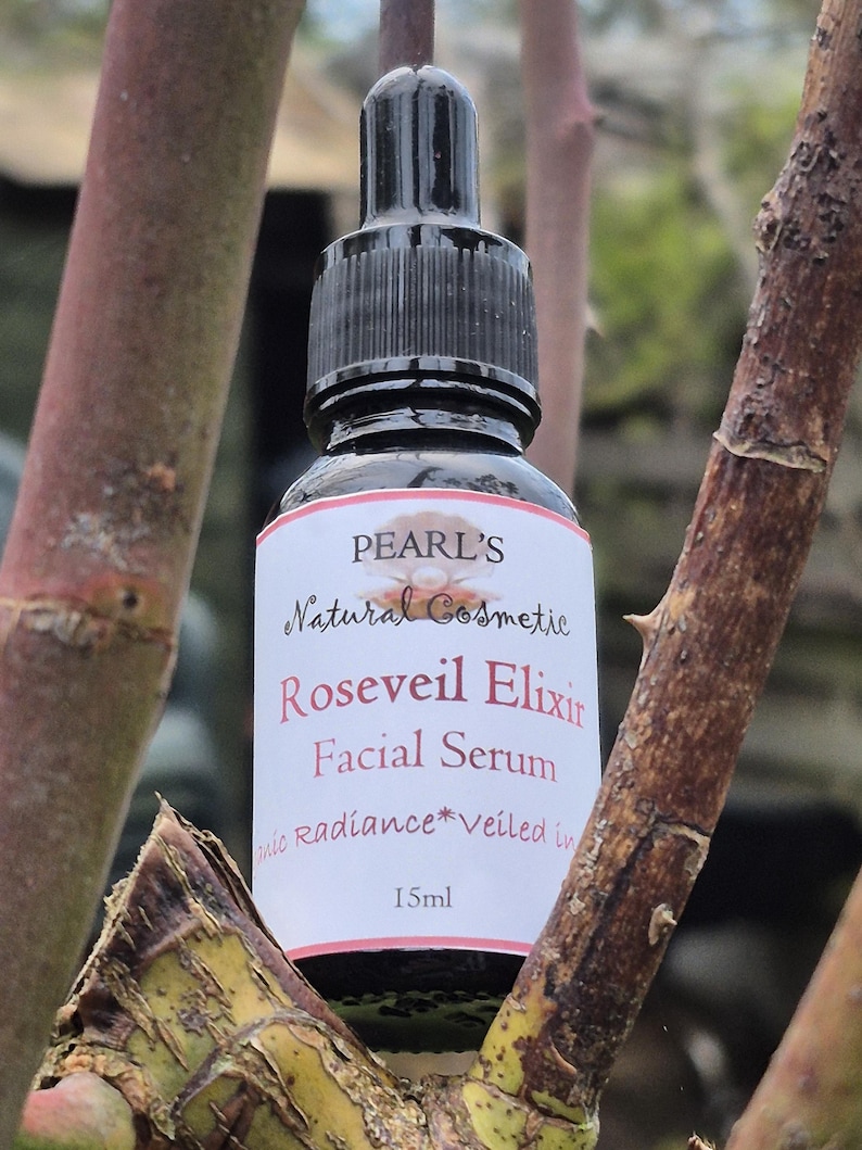 May include: A black dropper bottle of Pearl's Roseveil Elixir Facial Serum, 15ml. The label is white with red and black text. The bottle is surrounded by brown tree branches.