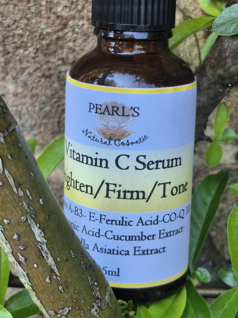 May include: A brown glass bottle of Pearl's Vitamin C Serum. The label is light blue and yellow with text that reads "Vitamin C Serum Brighten/Firm/Tone". The bottle is surrounded by green leaves.