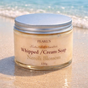 May include: A clear glass jar containing light beige whipped cream soap with a silver metal lid. The label reads PEARL'S Natural Cosmetic Whipped / Cream Soap Neroli Blossom 150g. The jar has a smooth texture and is filled to the top with product.