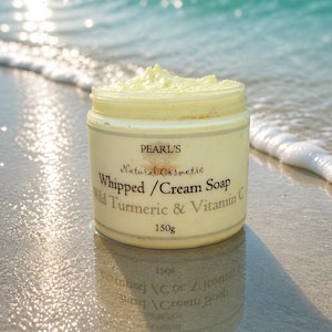 Può includere: Un barattolo rotondo in plastica contenente sapone in crema montato di colore giallo pallido. L'etichetta riporta Pearl's Natural Cosmetic, Whipped/Cream Soap, Wild Turmeric & Vitamin C, 150g. Il barattolo ha una superficie superiore texturizzata.