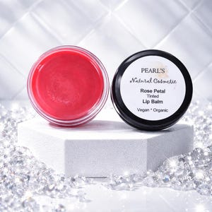 May include: Two small jars of lip balm. One jar is open, revealing a bright red balm. The other jar is closed with a black lid and a white label that reads "PEARL'S Natural Cosmetic Rose Petal Tinted Lip Balm Vegan * Organic."