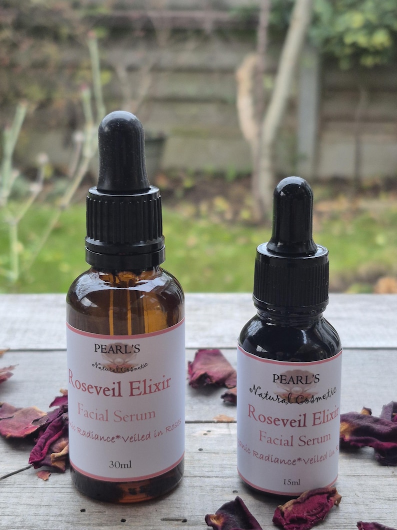 May include: Two brown glass bottles of facial serum with black droppers. The labels read "PEARL'S Natural Cosmetic Roseveil Elixir Facial Serum Radiance veiled in Rose". One bottle is 30ml, the other is 15ml. Dried rose petals are scattered around the bottles.