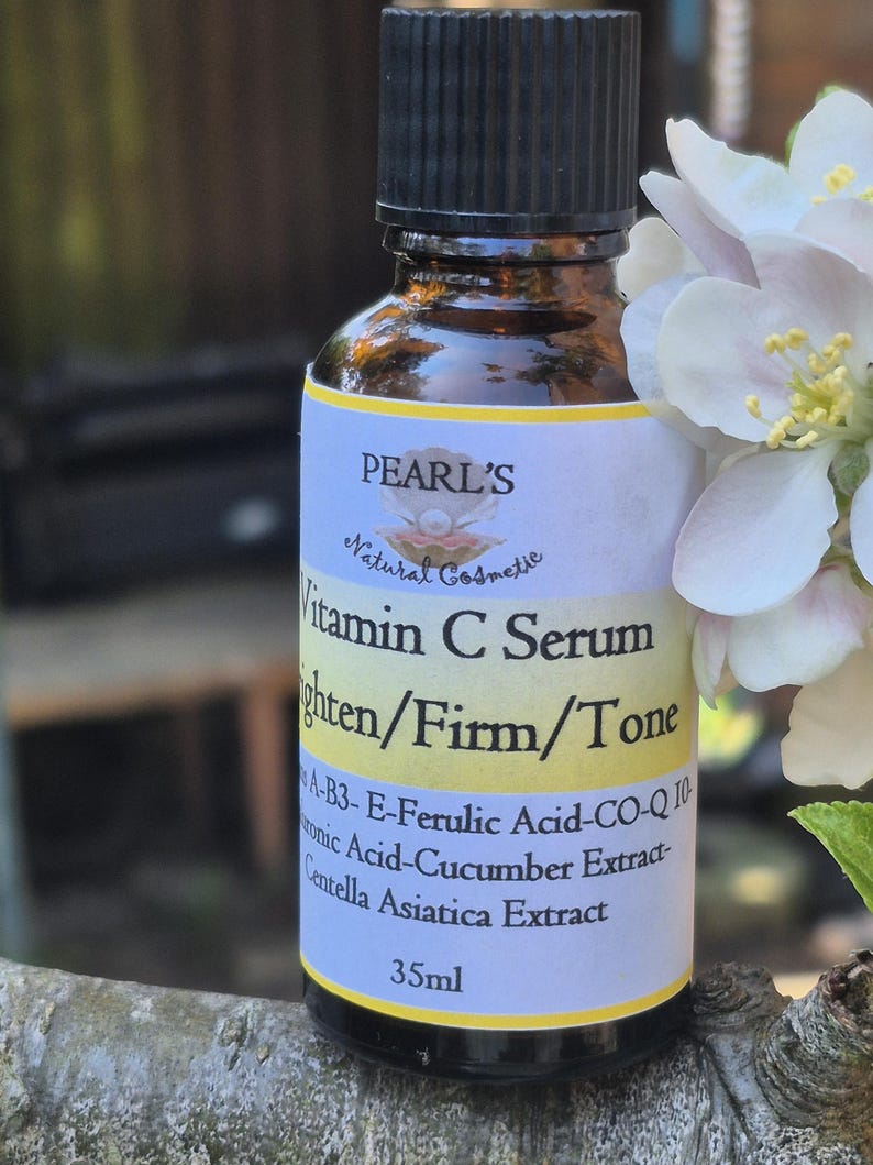 May include: A brown glass bottle of Pearl's Vitamin C Serum with a black cap. The label reads "Vitamin C Serum Brighten/Firm/Tone" and lists ingredients. The bottle is 35ml and is next to white flowers.