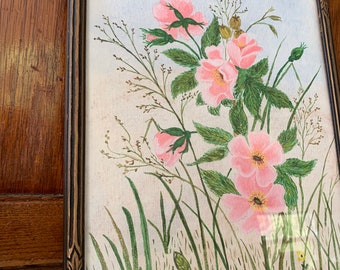 Op de afbeelding: Een ingelijst schilderij van roze bloemen met groene bladeren en stengels tegen een lichtblauwe achtergrond. De bloemen staan in een vaas en het schilderij is in een eenvoudige houten lijst.