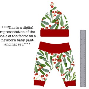 May include: A white and red baby hat and pants set with a holly berry and leaf pattern. The hat is a fold-over style and the pants have a red waistband and cuffs.
