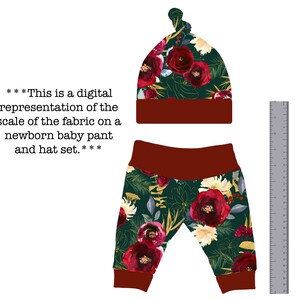 May include: A newborn baby hat and pants set with a burgundy red and green floral print. The hat has a knot on top and the pants have a burgundy red waistband.