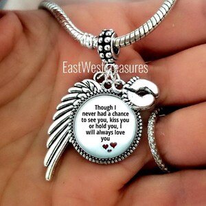 May include: Silver charm bracelet with a silver charm featuring a white background with the text "Though I never had a chance to see you, kiss you or hold you, I will always love you" and three red hearts. The charm is attached to a silver angel wing.