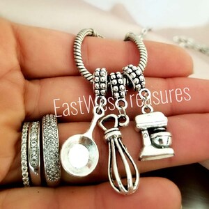 May include: Silver charm necklace with a spoon, whisk, and stand mixer charms. The charms are attached to a silver chain with a silver bead.