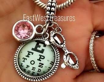 May include: Silver charm bracelet with a pink crystal, eye chart, and glasses charm. The charm is attached to a silver snake chain bracelet.