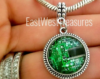 May include: A silver charm necklace with a round pendant featuring a green circuit board design. The pendant is surrounded by a silver beaded border.