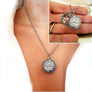 May include: A silver compass necklace with a locket that opens to reveal a photo. The locket is round and has a detailed compass design.