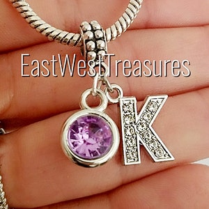 May include: A silver charm bracelet with a purple crystal charm and a silver charm with the letter K encrusted with clear crystals.
