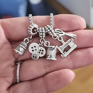 May include: Silver charm bracelet with sewing themed charms, including a thimble, buttons, a spool of thread, and a sewing machine.