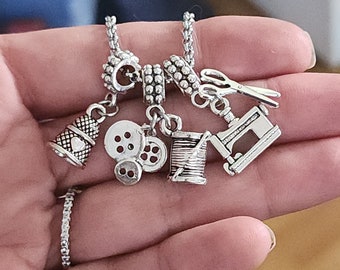 May include: Silver charm bracelet with sewing themed charms, including a thimble, buttons, a spool of thread, and a sewing machine.