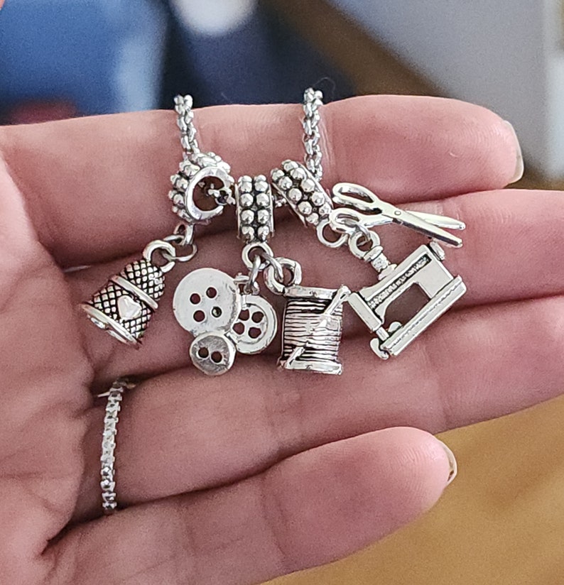 May include: Silver charm bracelet with sewing themed charms, including a thimble, buttons, a spool of thread, and a sewing machine.