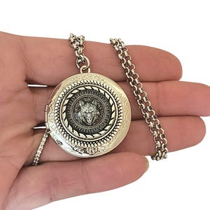 May include: Silver locket necklace with a wolf head design. The locket has a detailed engraved border and a chain.