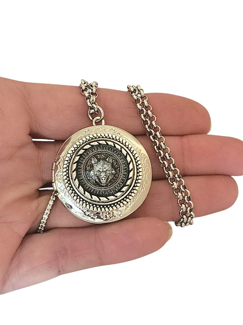May include: Silver locket necklace with a wolf head design. The locket has a detailed engraved border and a chain.
