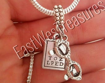 May include: Silver charm necklace with a silver eye chart charm and a pair of glasses charm. The eye chart says "TOZ LPED".