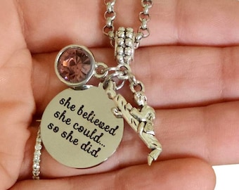 May include: Silver necklace with a charm that says "she believed she could... so she did". The charm is attached to a silver chain with a pink crystal bead.