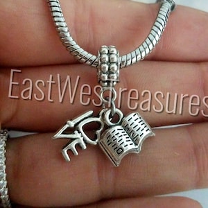 May include: Silver charm bracelet with a charm that says "I love" and has a small heart, and a charm that is an open book.