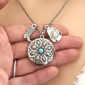 May include: Silver-toned necklace with a round locket pendant, a turquoise stone, and cowboy-themed charms. The locket has a detailed floral design. Charms include a cowboy boot and a cowboy hat.