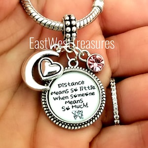 May include: Silver charm bracelet with a silver charm that says "Distance means so little when someone means so much!" with a silver crescent moon and heart charm, and a pink crystal charm.