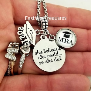 Peut inclure: Un collier de charme argenté avec un charme de chapeau de graduation, un charme avec l'année 2021, un charme avec le texte "she believed she could... so she did", un charme avec le texte "MBA" et un chapeau de graduation, et un charme avec une lettre H avec des strass.