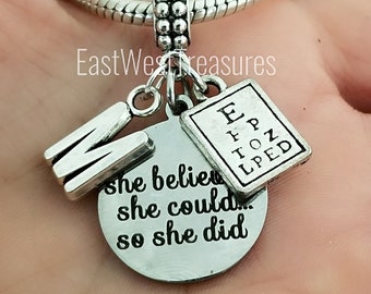 May include: Silver charm bracelet with a silver charm that says "She believed she could so she did". The charm is attached to a silver chain with a silver eye chart charm and a silver letter "M" charm.