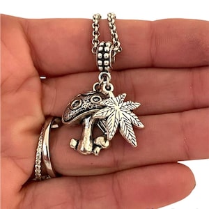 May include: Silver necklace with a mushroom and marijuana leaf charm. The charm is detailed and has a vintage look.