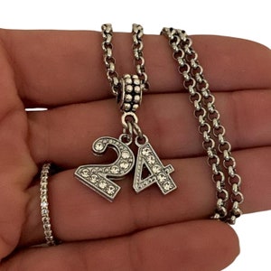 May include: A silver chain necklace with a charm that says "24" in rhinestones.