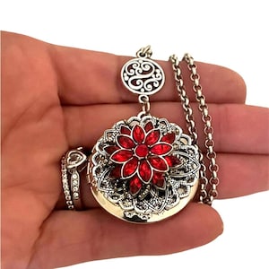May include: A silver locket necklace with a red jeweled flower design. The locket has a filigree pattern and a chain with a decorative charm.