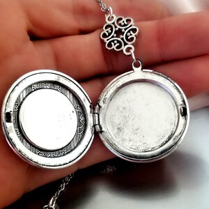 May include: Silver locket necklace with a filigree design. The locket is open, revealing a blank interior. The necklace has a delicate chain.