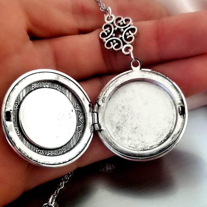 May include: Silver locket necklace with a filigree design. The locket is open, revealing a blank interior. The necklace has a delicate chain.