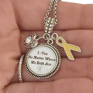 May include: A silver charm necklace with a round charm that says "I love you no matter where we both are". The charm also features a small pink heart and a yellow ribbon.