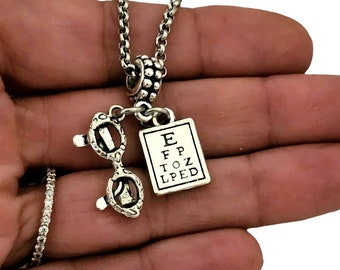 May include: Silver necklace with a charm of an eye chart and a pair of glasses. The eye chart reads "E F P T O Z L P E D".