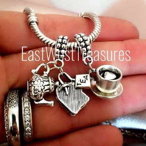 May include: Silver charm bracelet with tea-themed charms, including a teapot, tea bag, and teacup. The charms are attached to a silver snake chain bracelet.