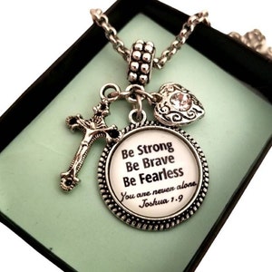 May include: Silver necklace with a charm that says "Be Strong Be Brave Be Fearless You are never alone Joshua 1:9". The charm is attached to a silver cross and a silver heart with a rhinestone.