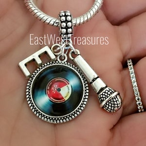 May include: Silver charm bracelet with a microphone, a record, and a letter 'E' charm. The record charm has a blue and red design.