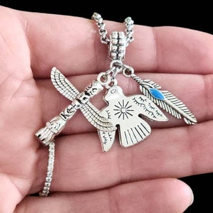 May include: Silver necklace with three charms: a totem pole, a bird, and a feather with a blue accent.