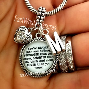 May include: Silver charm bracelet with a heart charm, a letter M charm, and a round charm with the text "You're BRAVER than you believe, STRONGER than you seem, SMARTER than you think and more LOVED than you know."