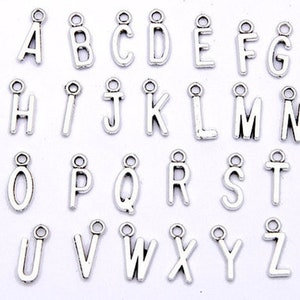 May include: Silver-colored alphabet charms, each with a small loop at the top for stringing. The letters A through Z are displayed, perfect for personalized jewelry or craft projects. The charms are arranged in rows.