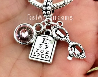 May include: Silver charm bracelet with a pink crystal, eye chart, and glasses charm. The eye chart charm has the letters E, FP, TOZ, and LPED.