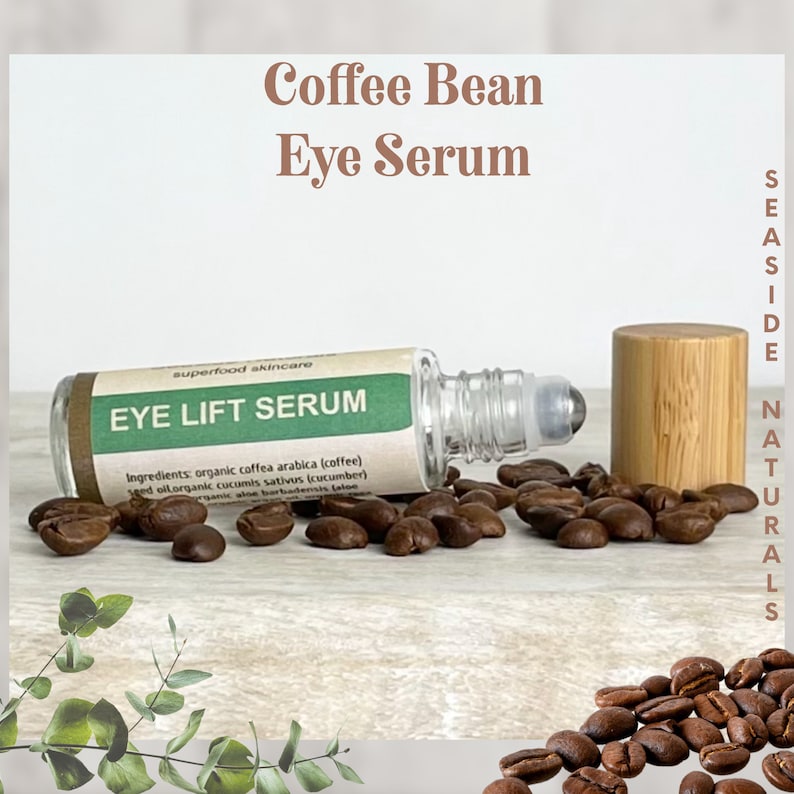 Puede incluir: Un frasco de vidrio con rodillo para s&eacute;rum para ojos con una etiqueta verde que dice "EYE LIFT SERUM" y "superfood skincare". El frasco est&aacute; rodeado de granos de caf&eacute; y una tapa de rodillo de madera. La etiqueta tambi&eacute;n enumera los ingredientes: coffea arabica org&aacute;nica (caf&eacute;), aceite de semilla org&aacute;nica de cucumis sativus (pepino), aloe barbadensis org&aacute;nico (aloe).