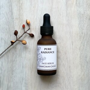 May include: A brown glass bottle with a black dropper top. The bottle is labeled "PURE RADIANCE FACE SERUM HYDRATE | NOURISH | RESTORE".