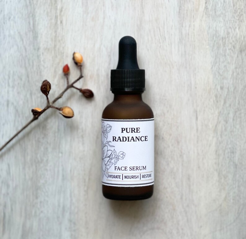 May include: A brown glass bottle with a black dropper top. The bottle is labeled "PURE RADIANCE FACE SERUM HYDRATE | NOURISH | RESTORE".