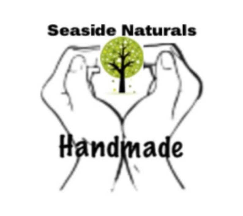 May include: A black and white illustration of two hands forming a heart shape around a green tree with the text "Seaside Naturals Handmade" below.